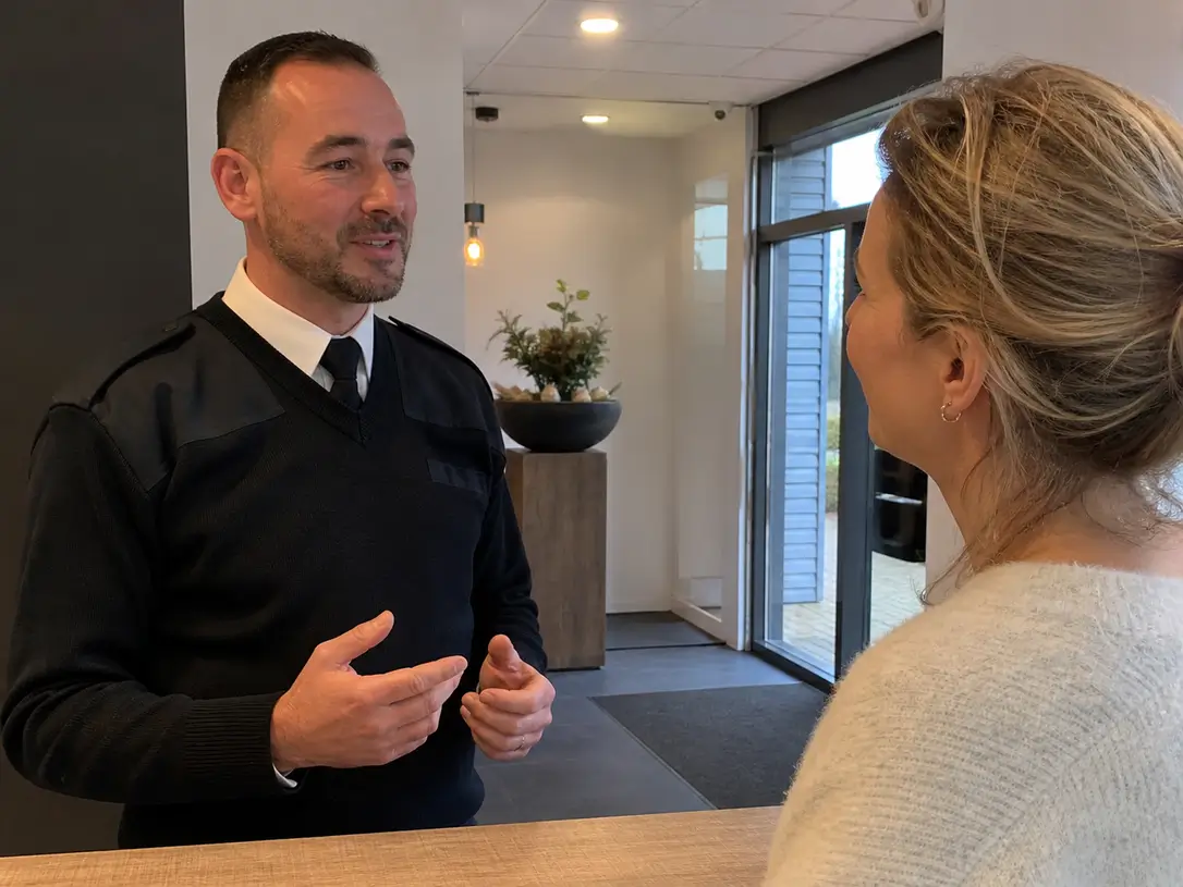 Beveiliger legt met een glimlach iets uit aan een vrouw als potentiële klant