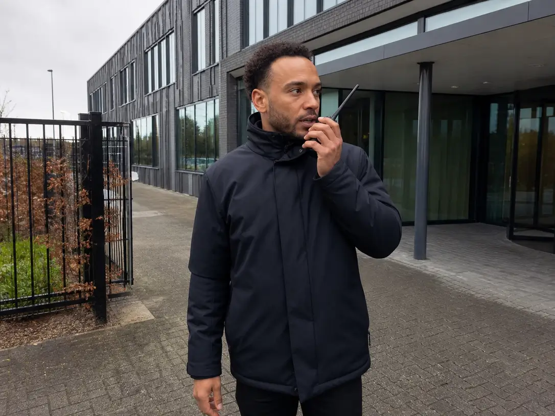 Beveiliger met portofoon staat waakzaam bij de ingang van een gebouw