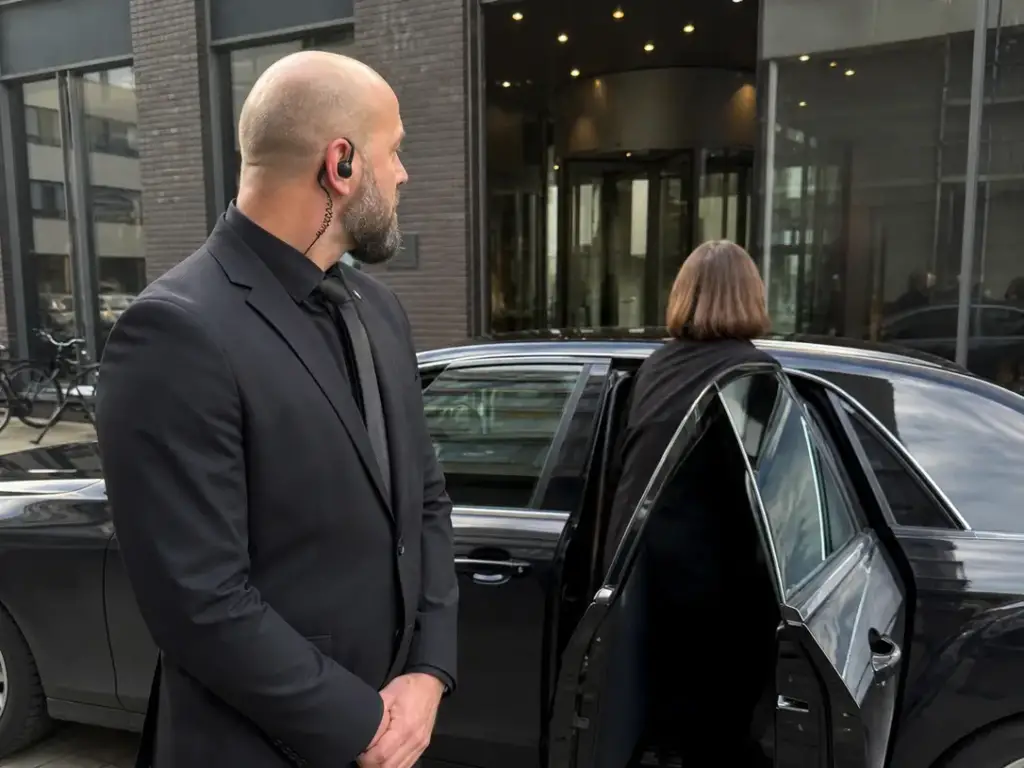 Beveiliger begeleidt een vrouw bij het instappen in een auto voor een gebouw